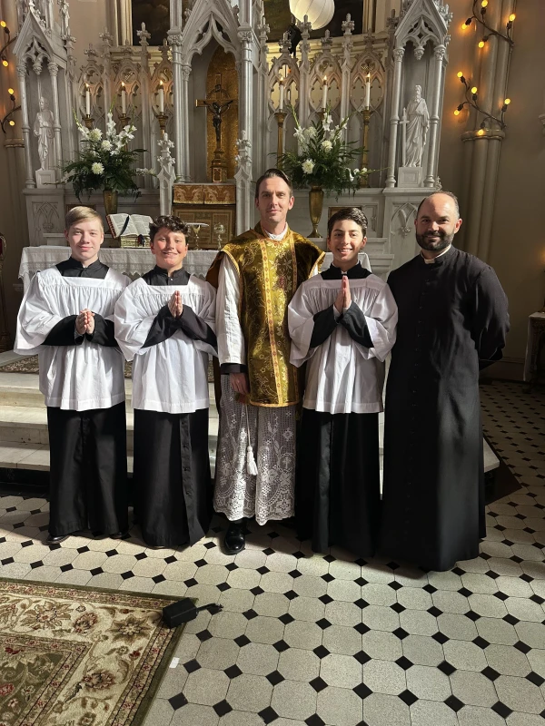 El P. Aaron Williams, rector de la Basílica de St. Mary en Natchez, con sotana, junto al actor Dan Stevens y algunos de los monaguillos que participaron en la película. Crédito: Cortesía del P. Aaron Williams.